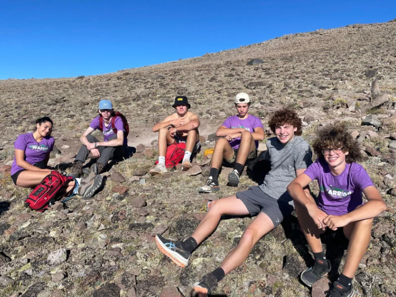 A group of teen hikers resting on the summit of Mount Rose during the 2023 Be Warrior Challenge Hike