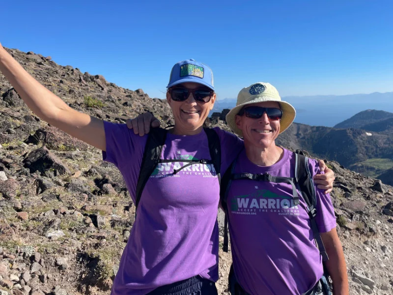 A man and woman celebrate reaching the summit of Mount Rose during the 2023 Be Warrior Challenge Hike