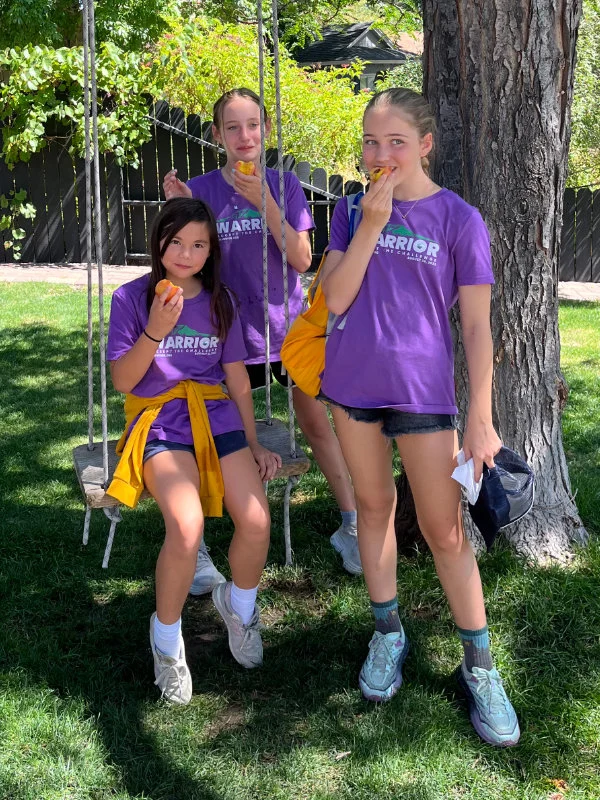 Three girls relax in a park after the 2023 Be Warrior Challenge Hike