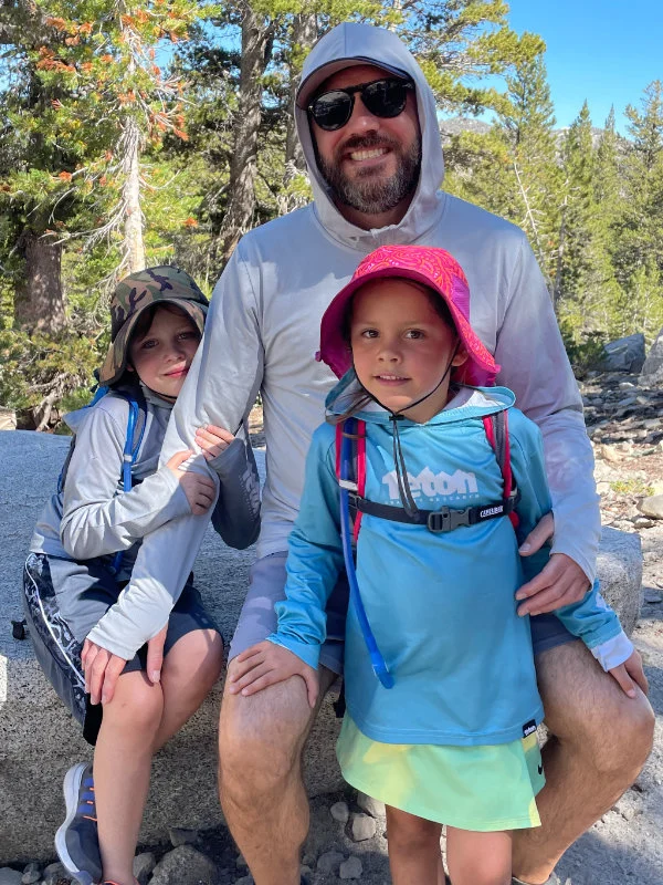 A man and two children rest together on a rock during the 2023 Be Warrior Challenge Hike